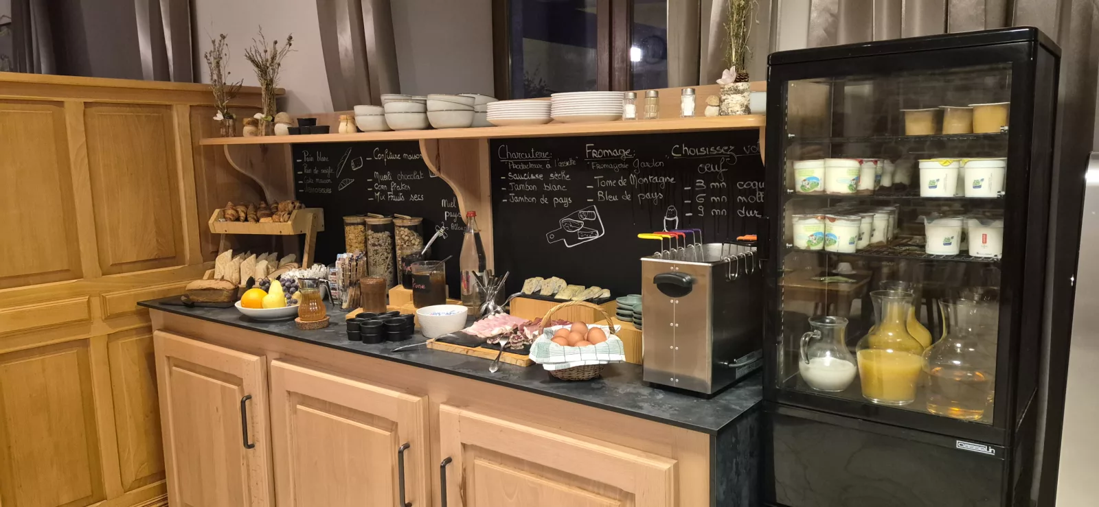 Le buffet du petit-déjeuner et son tableau noir, avec le cuiseur à œufs et la vitrine de yaourts, lait et jus de fruits