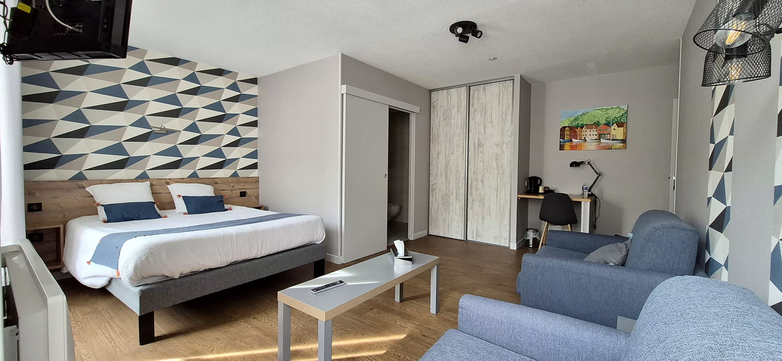 Chambre bleue : grand lit, papier peint géométrique, canapés et bureau