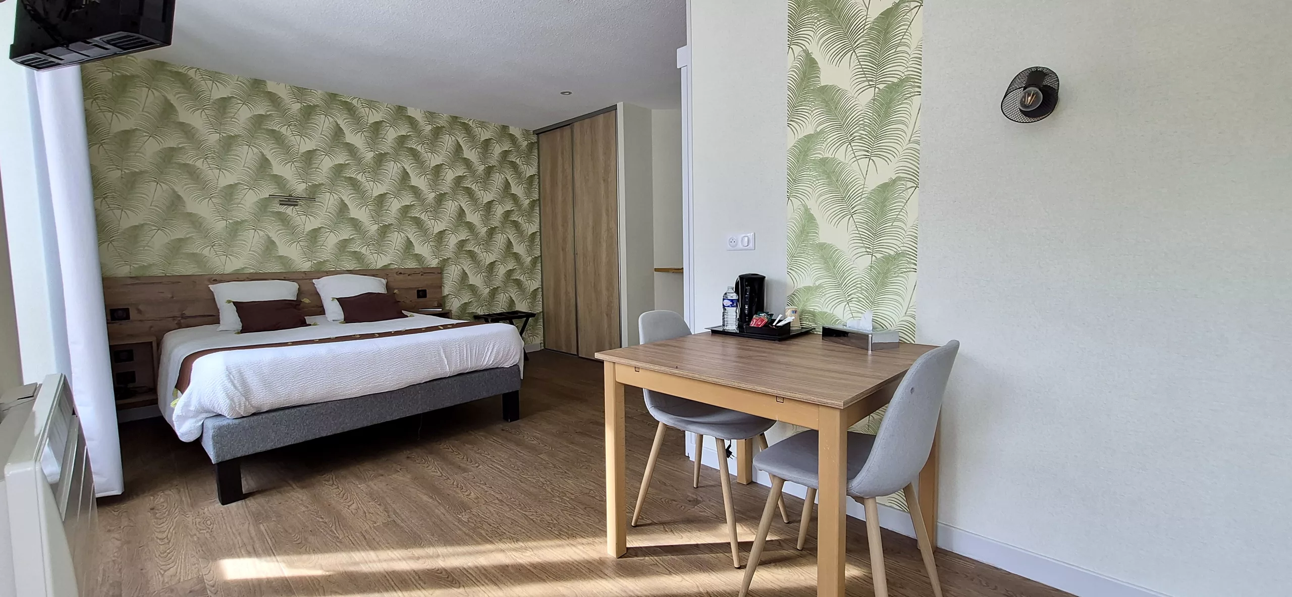 Chambre au papier peint feuillage, grand lit et table pour deux