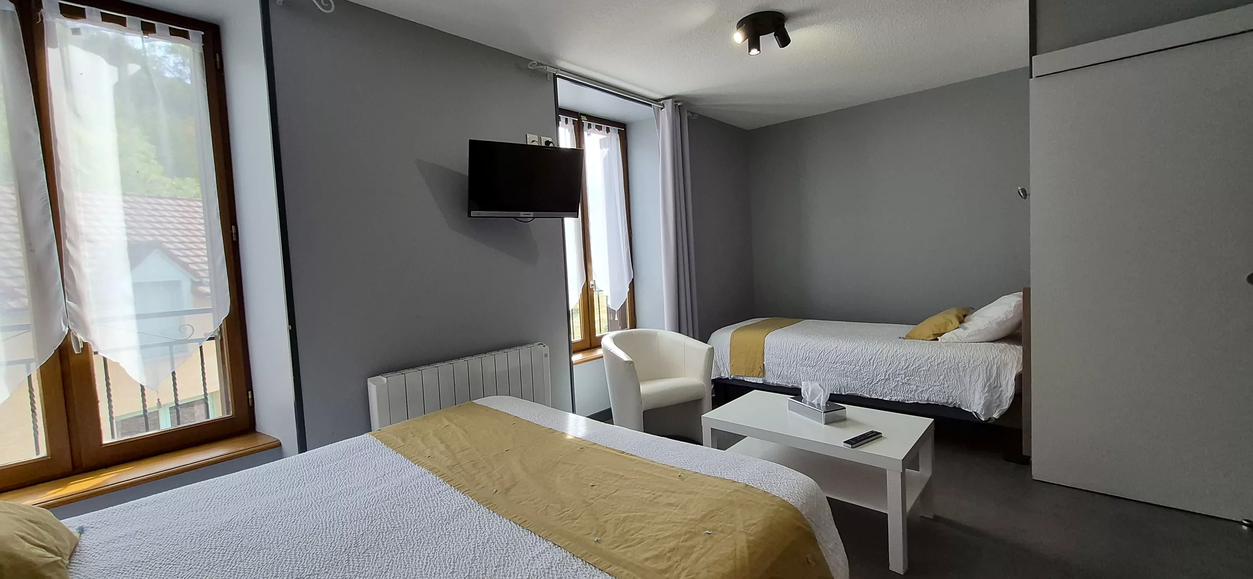 Chambre grise avec lit double, lit simple et fauteuil, jetés moutarde
