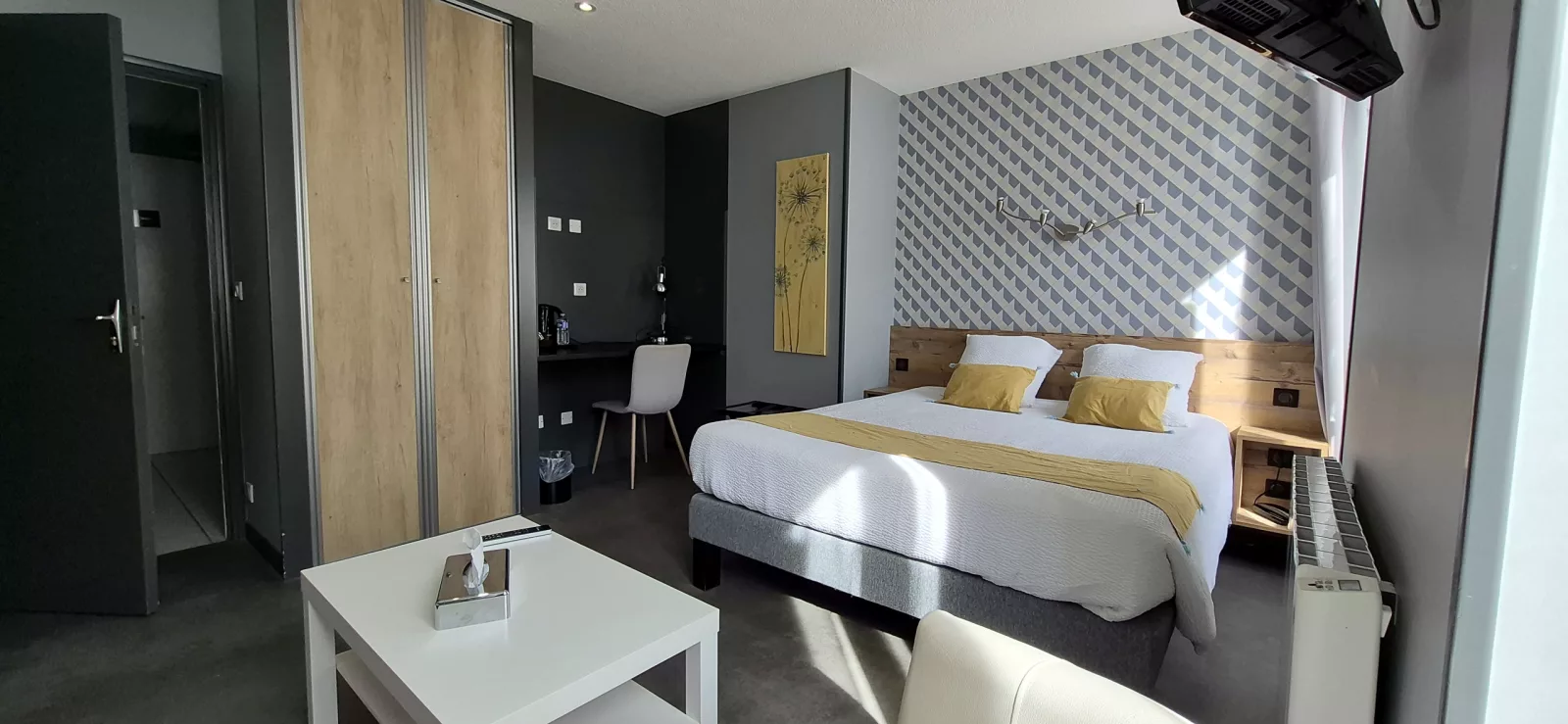 Chambre lumineuse aux tons gris et jaunes, grand lit et bureau