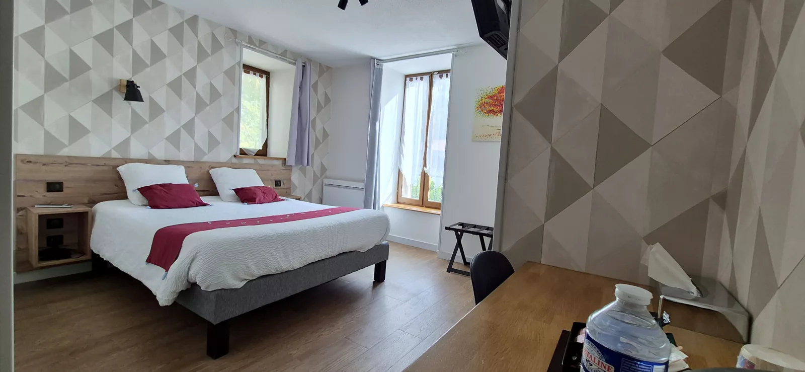 Chambre aux tons beiges et bordeaux, grand lit et deux fenêtres