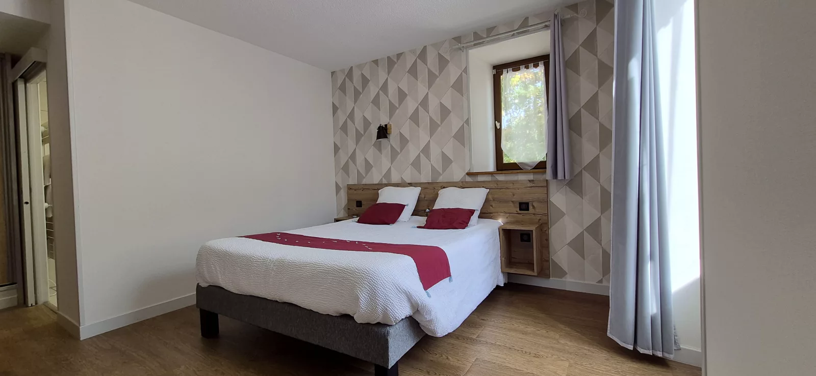Chambre aux tons beiges et bordeaux, tête de lit en bois et vue sur la verdure