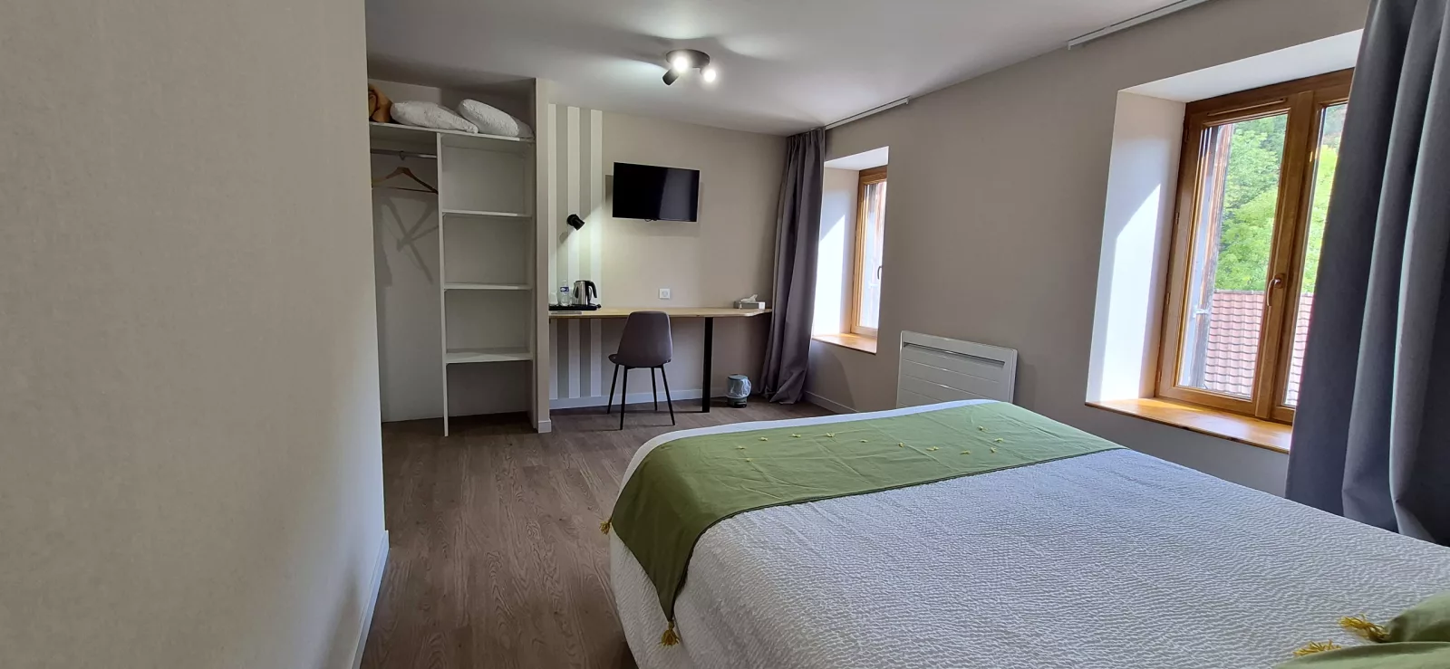 Chambre aux tons verts, bureau, penderie ouverte et fenêtres sur le village