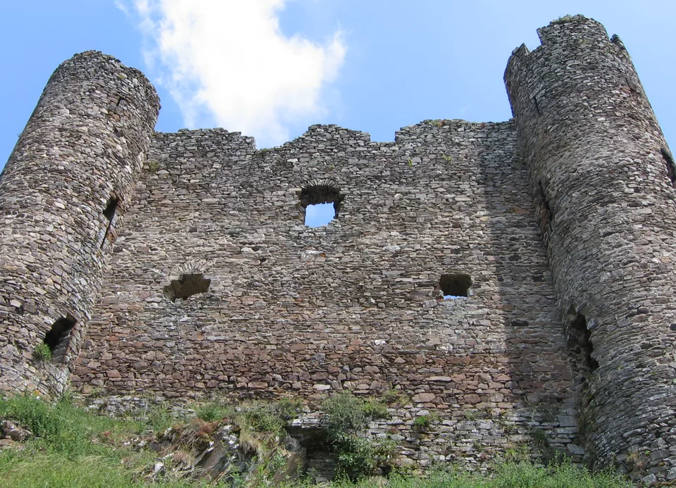 The ruins of Alleuze castle on a green peak, reflected in the water