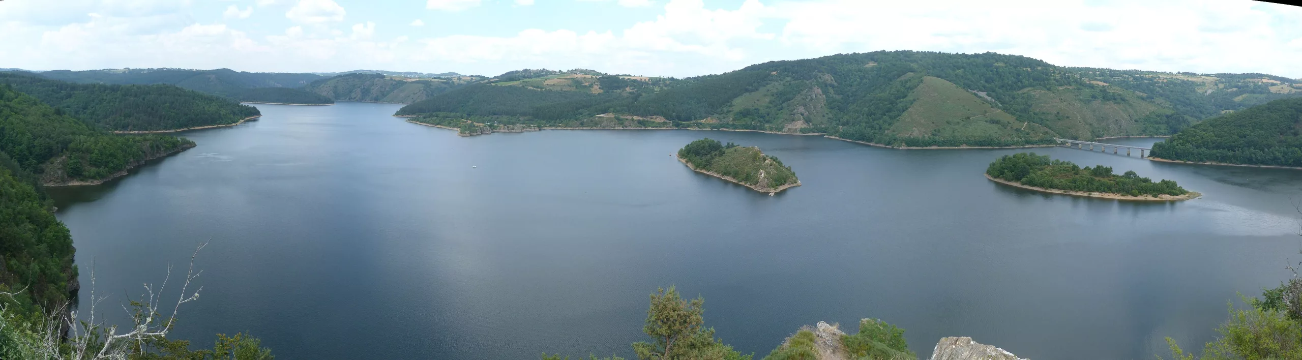 Grandval lake winding between wooded hills, with the arched dam