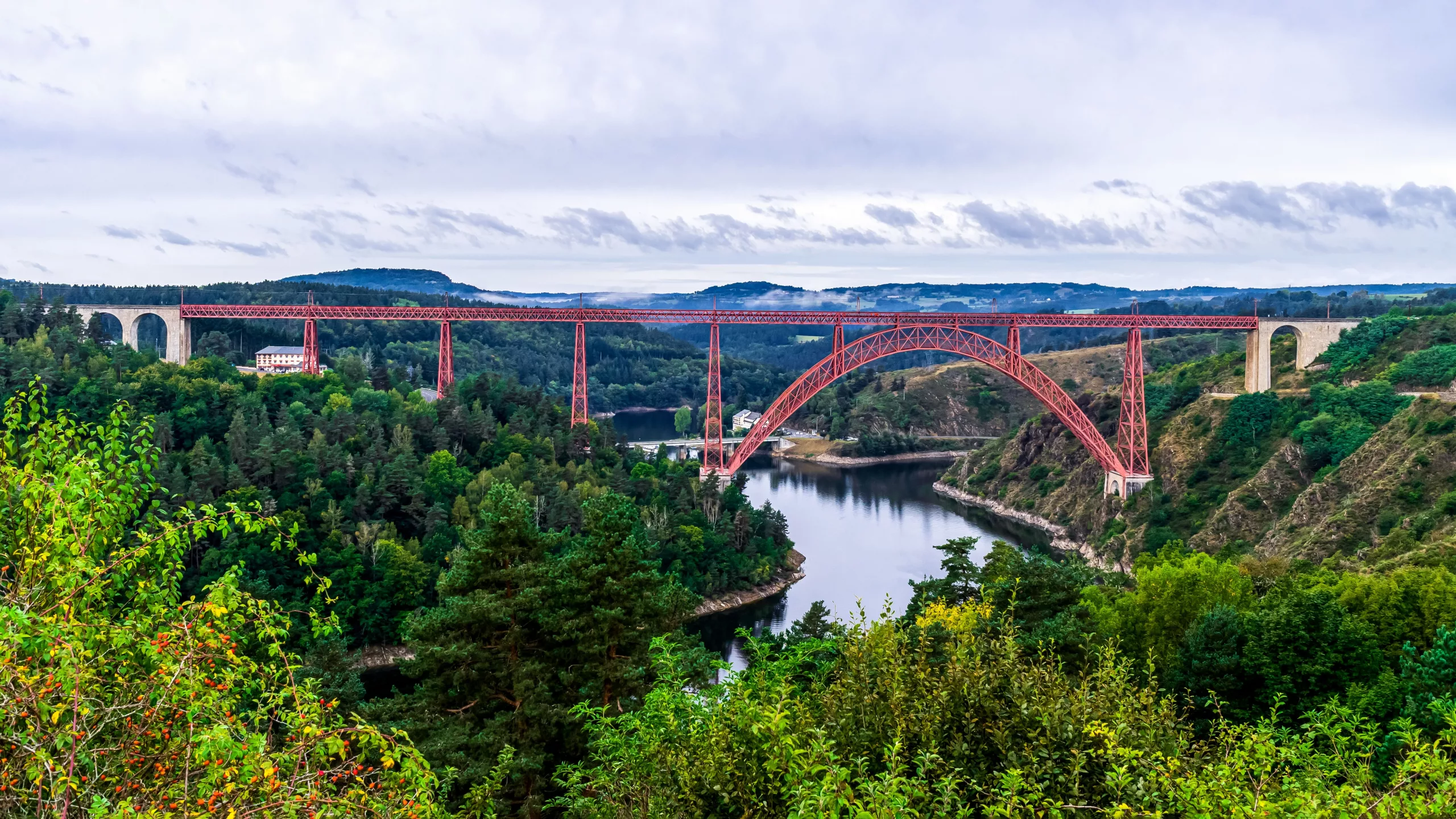 The Garabit viaduct, a red metal arch above the lake, surrounded by forest