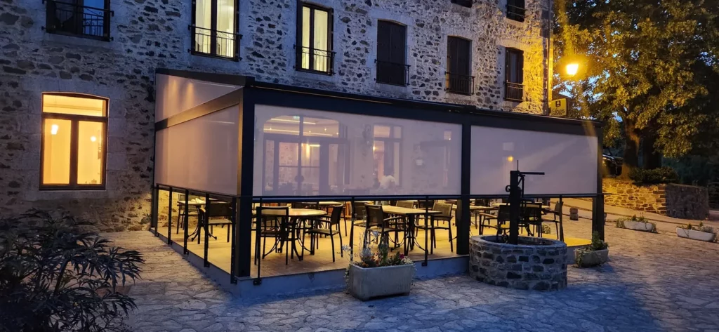 La nouvelle terrasse couverte de l'auberge, éclairée le soir au pied de la façade en pierre